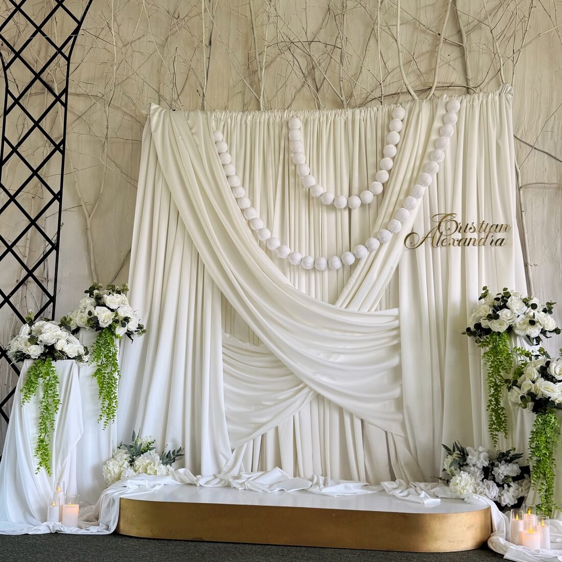 Photocorner de nuntă cu draperii crem, ghirlande de perle și aranjamente florale albe